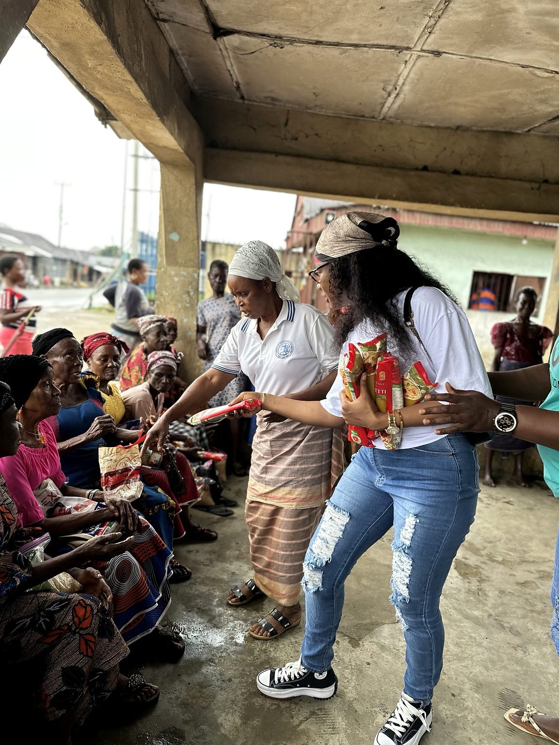 Women hand packets of food to older women seated together.